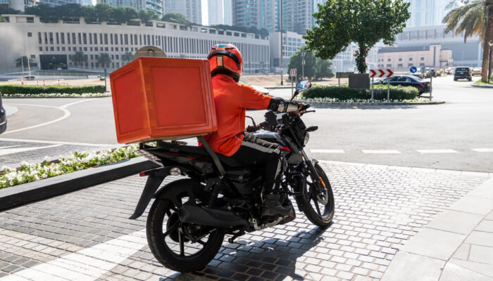 Coursier moto avec top-case orange en livraison express en Île-de-France